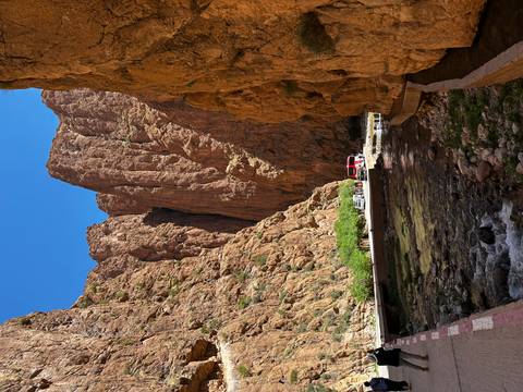       Steep red rock walls of Todra Gorge tower over a small stream and tourists
  