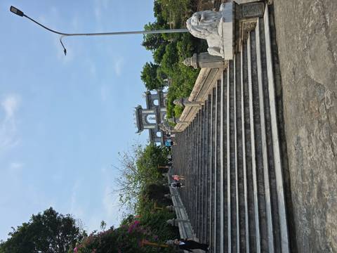       Long stone stairs lead up to an ornate hilltop gateway surrounded by greenery under a clear sky.
  