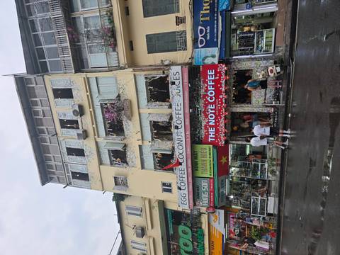       A colorful coffee shop plastered with sticky notes stands on a busy Hanoi street after rain.
  