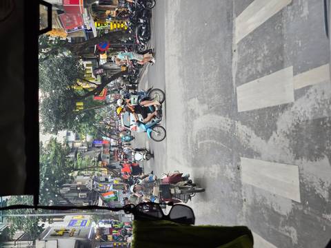       Motorbikes weave through a narrow Hanoi Old Quarter street filled with flags and storefronts.
  