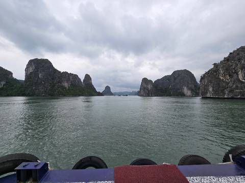       Dramatic limestone karsts rise from calm green waters under a cloudy sky in Halong Bay.
  