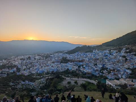       Wide sunset panorama of a mountain-ringed valley town with distinctive blue buildings.
  
