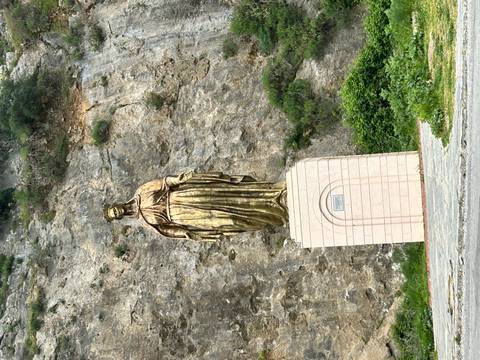       Gold-toned statue of the Virgin Mary set against a rocky hillside.
  