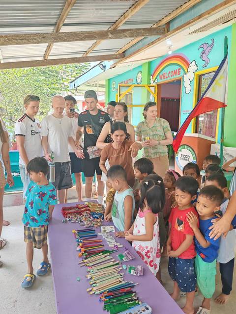       Travellers distribute snacks to local children inside a brightly painted community building.
  