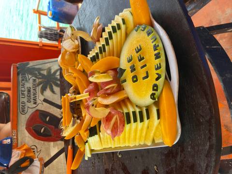       Vertical platter of carved tropical fruit on a boat table reading 'I ♥ ONE LIFE ADVENTURES'.
  