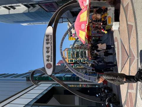       Crowds enter the BUSAN International Film Festival street under modern archways.
  