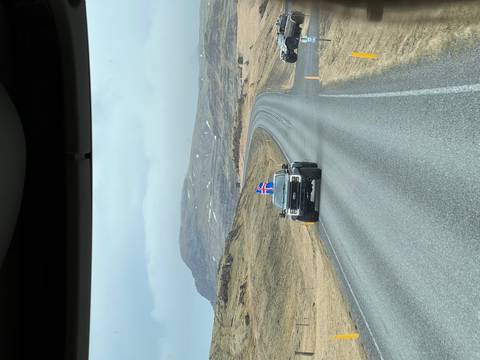       Icelandic road stretches through barren highlands with a truck flying the national flag.
  