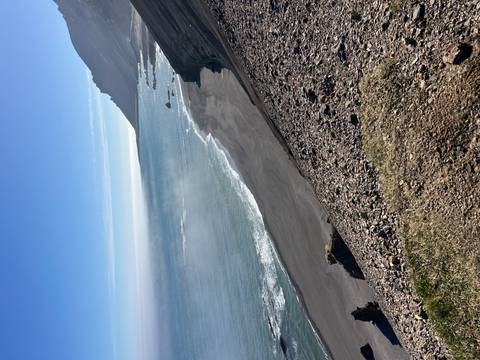       Black-sand beach curves below misty cliffs along Iceland’s east coast.
  