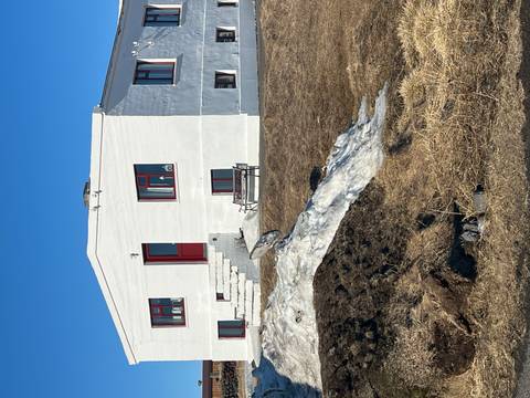       Simple white farmhouse with red trim set against dry grass and lingering snow.
  