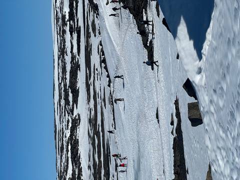       Travellers walk across a vast snowy landscape dotted with rocks and fences.
  