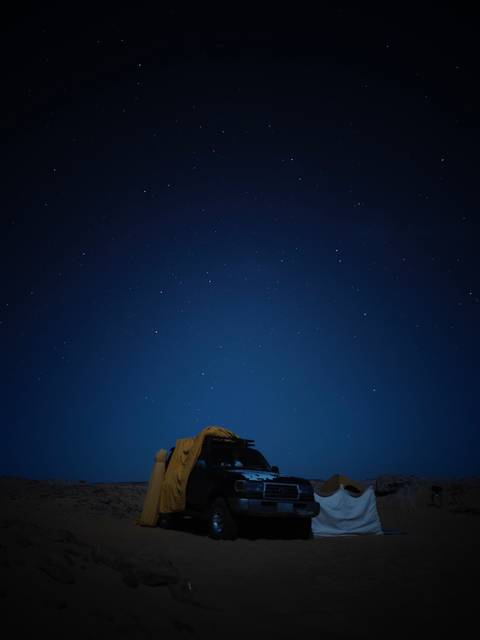       Star-filled night sky above a low desert camp silhouette
  