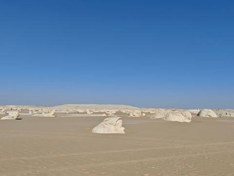       Surreal white limestone formations dotting an expansive desert under cloudless blue skies
  