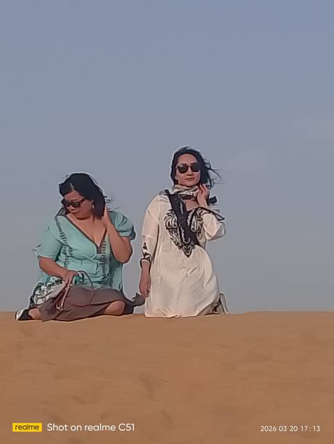       Two women with wind-swept hair riding through the desert wearing sunglasses
  