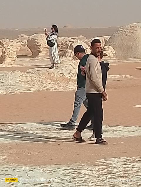       People walking by eroded white rock formations on sandy ground
  