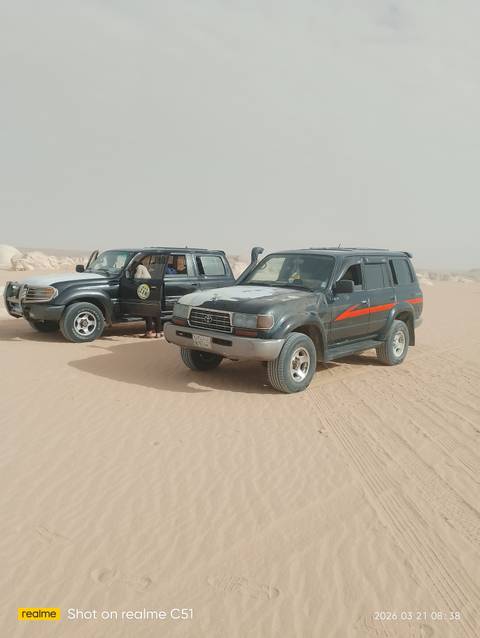       Two rugged 4x4 vehicles parked on desert sand with a passenger entering
  