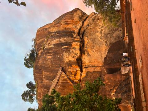       Massive orange rock fortress with steep staircase glowing in soft dawn light
  