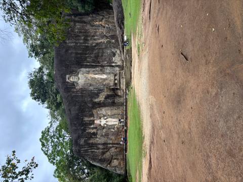       Ancient rock face with large standing Buddha carvings surrounded by greenery
  