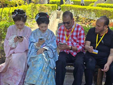       Two tourists seated with women in traditional hanfu, all focused on their phones
  