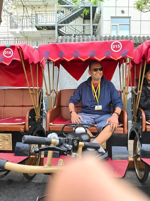       Smiling traveller sitting in a red-canopied cycle rickshaw
  