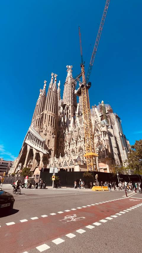       Iconic spires of the Sagrada Família under bright blue Barcelona sky with construction crane
  