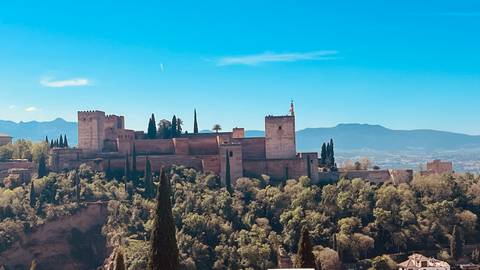       Majestic Alhambra fortress complex rising above forested hills with mountains beyond
  