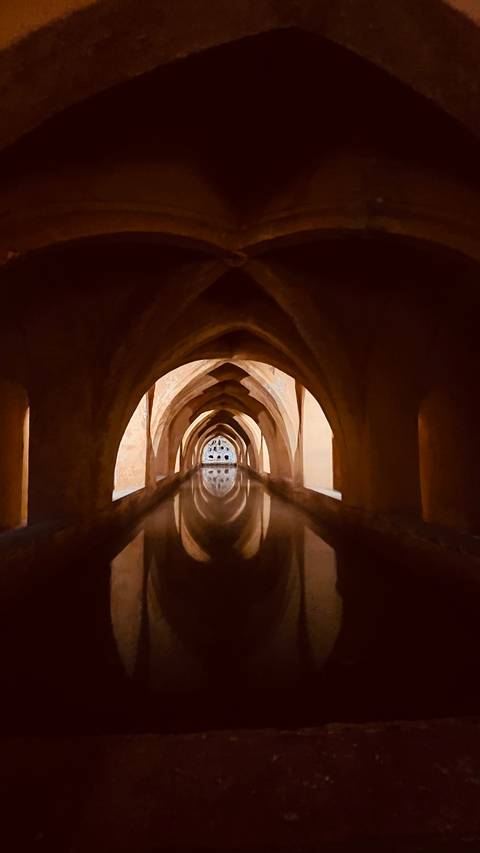       Arched underground chamber with still water reflecting repeating gothic-style vaults.
  