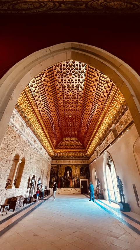       Intricately carved and illuminated wooden ceiling in a historic hall.
  