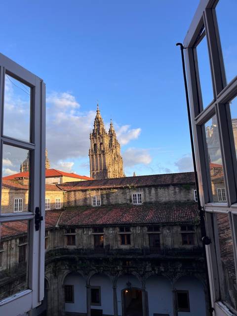       Gothic cathedral towers of Santiago de Compostela framed by an open window at sunrise light.
  