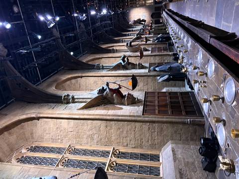       Long banquet tables with gilt tableware inside a grand medieval-style hall adorned with gargoyle statues and high arched windows
  