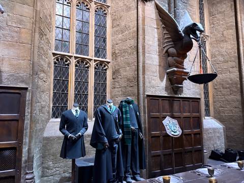       Display of Hogwarts school uniforms on mannequins beside stone walls and stained-glass windows
  