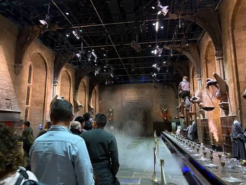       Visitors walking through a mist-filled great hall set with long tables and gargoyles overhead
  