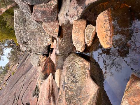       Still pool reflecting rugged granite slabs and scattered trees in bushland
  