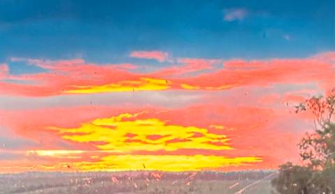       Vivid orange and pink sunset clouds over distant horizon, photographed through a streaked window
  
