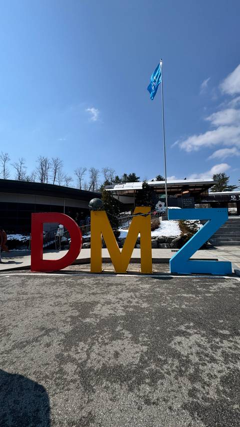       Large colorful 3-D letters spelling ‘DMZ’ outside a visitor center with snow on the ground and blue sky.
  