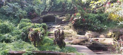       Lush tropical garden with mossy stone terraces and a carved cave opening.
  