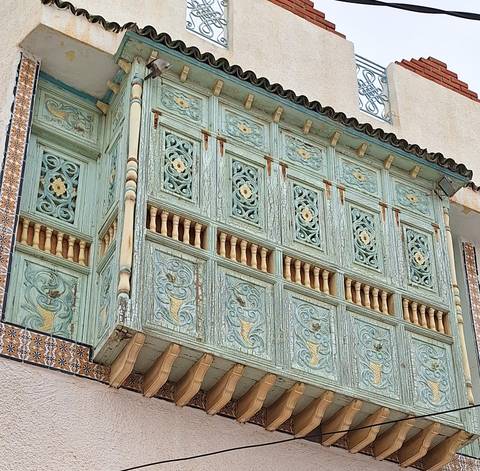       Close view of ornate mint-green wooden mashrabiya balcony with Tunisian tile work.
  