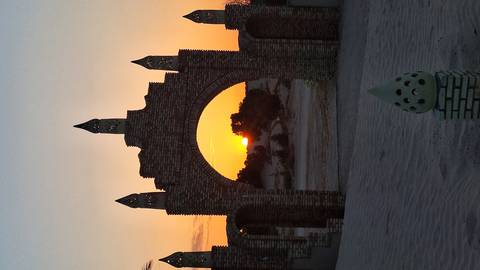       Brick archway framing an orange sun descending over desert dunes.
  