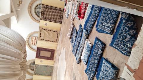       Interior hall with rolled woven carpets arranged on the floor beneath draped ceiling fabric.
  