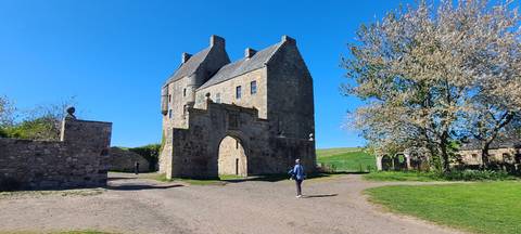       Historic Doune Castle gatehouse framed by bright blue sky and spring blossoms with a visitor walking.
  