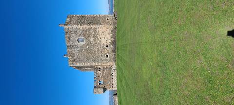       Square stone tower of Blackness Castle set on a vast green lawn under clear blue sky.
  