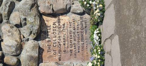       Engraved Culloden Battlefield memorial stone commemorating the 1746 battle surrounded by flowers.
  