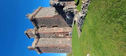       Close view of tall stone walls and towers of a ruined Scottish castle against vivid blue sky.
  