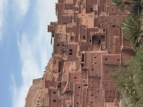       The earthen adobe buildings of Aït Benhaddou cascade down a hillside beneath a blue sky
  