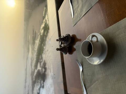       A cup of coffee and Moroccan condiments rest on a table overlooking a misty shoreline at dawn
  
