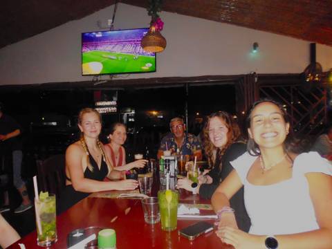       Friends enjoying drinks at an indoor restaurant with a TV showing sports overhead.
  