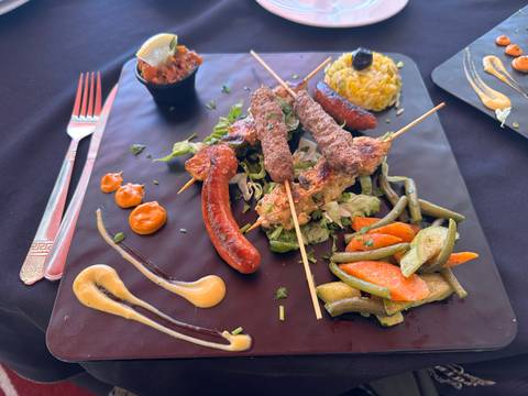       Plate of Moroccan mixed grill skewers with vegetables and colorful sauces arranged artfully.
  