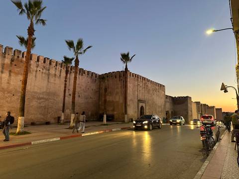      Medina defensive walls at dusk with cars and pedestrians moving along the lit street.
  