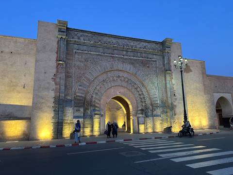       Illuminated Bab Mansour gate in Meknes glowing blue and gold against the twilight sky.
  