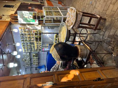       Street vendor preparing traditional Moroccan pastries beside stacked jars of preserved lemons.
  
