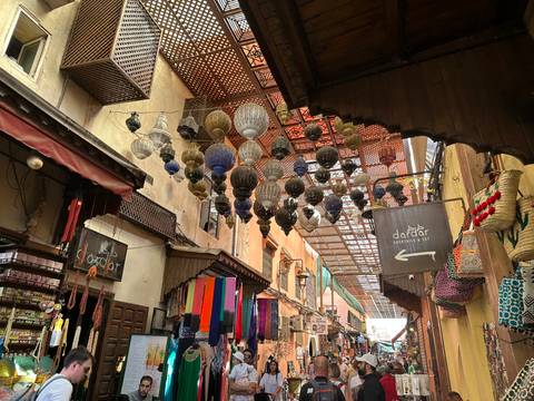       Narrow souk alley in Marrakesh decorated with hanging metal lanterns and colorful textiles.
  